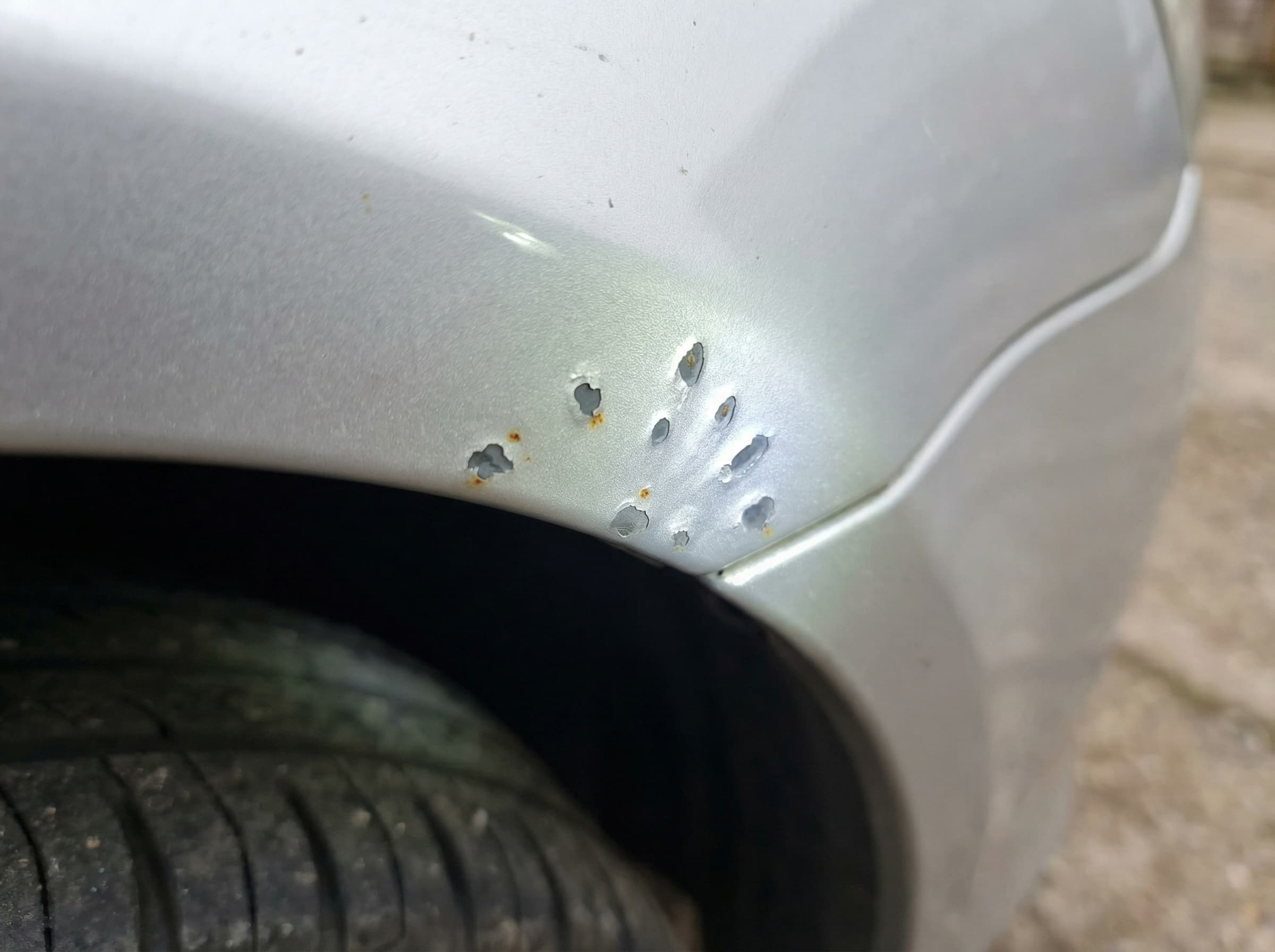Close-up of road debris damage on a silver car front guard